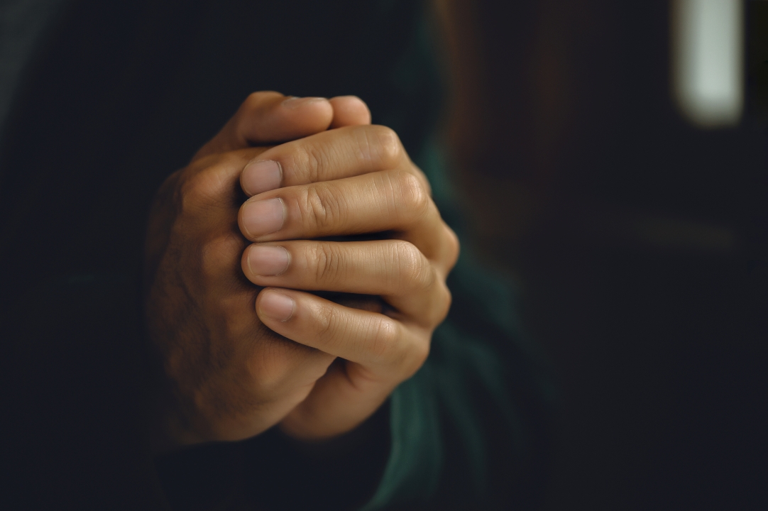 hands folded in prayer in dark room